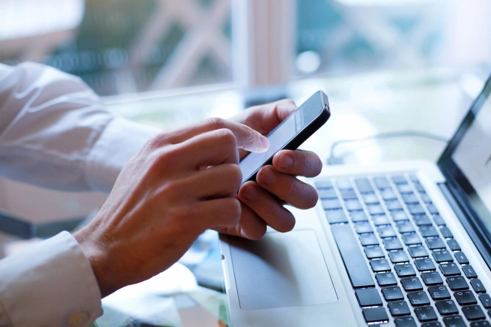 A person is using their cell phone while sitting at the computer.