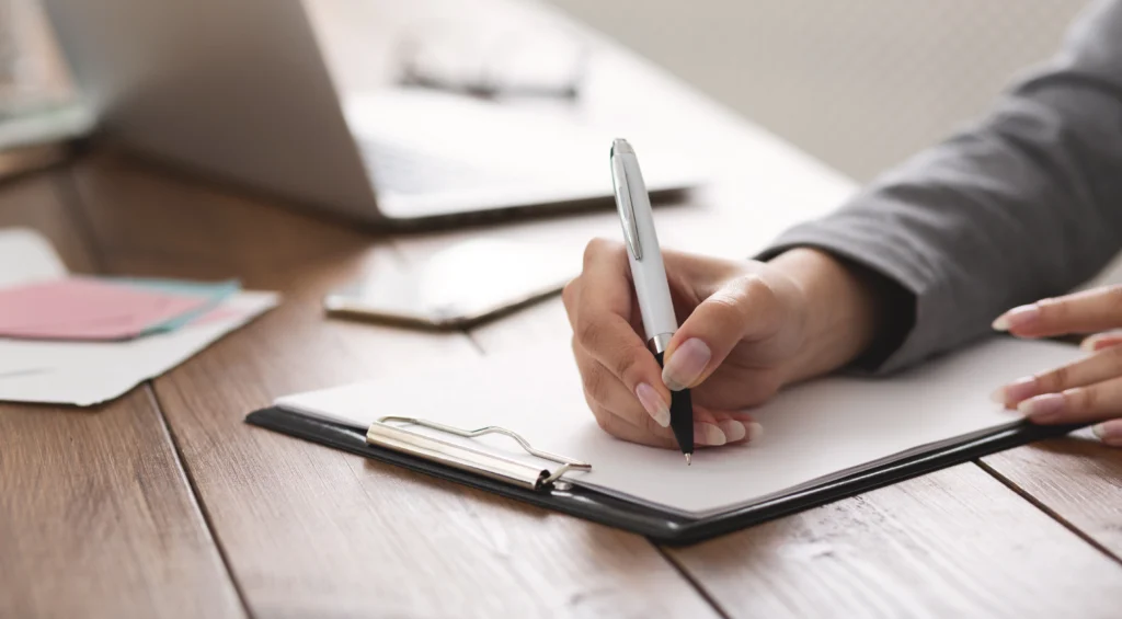 A person writing on paper with a pen.